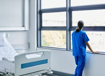 Young doctor looking out of window next to empty bed